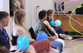 A group of people listening to a presentation, while holding blue ballons