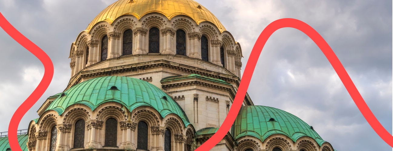 St. Alexander Nevsky Cathedral in Sofia, Bulgaria, featuring a grand dome with gold accents, multiple smaller domes, and ornate details on its facade, set against a backdrop of blue sky.