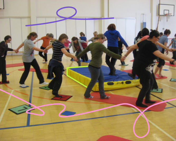 A group of people, holding hands, are moving in a circle, as if engaged in a dance or game.