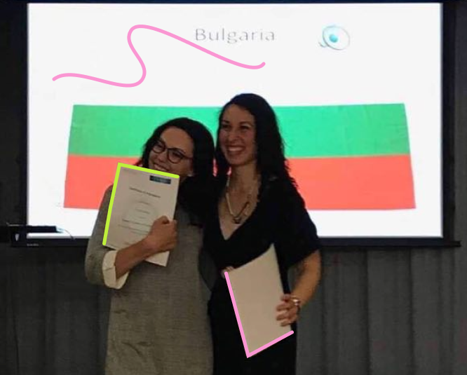 Two young women showing their diploma with a Bulgarian flag on the background